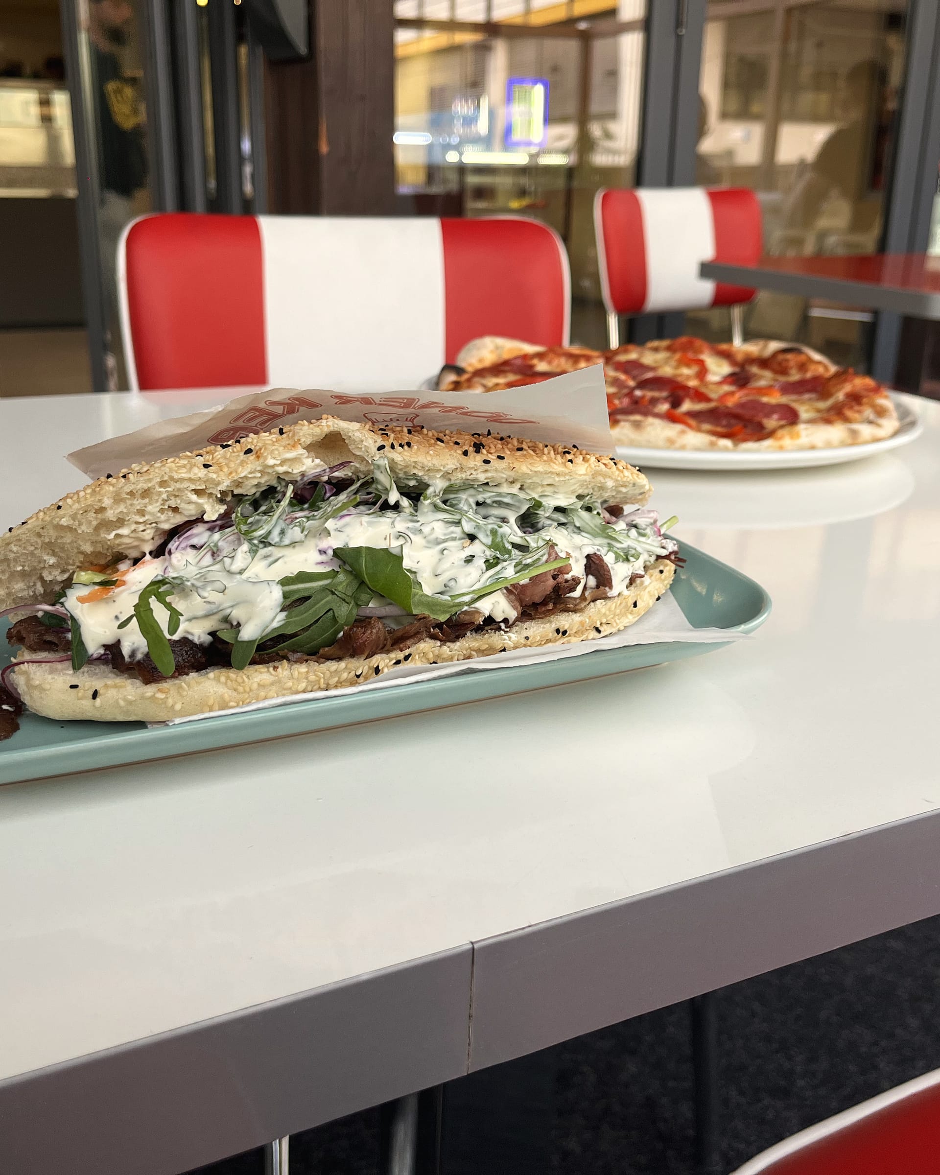 Steak-Döner-Sandwich, dahinter die rot-weißen Diner-Sitze von früher