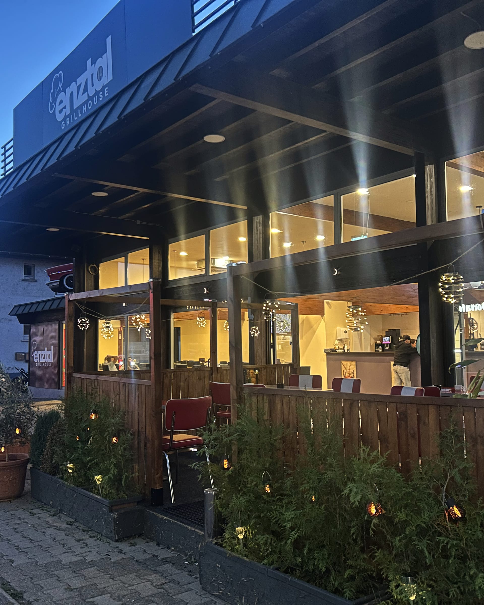 Die Terrasse des Enztal Grillhouse mit Holzzaun und Pflanzen am Abend